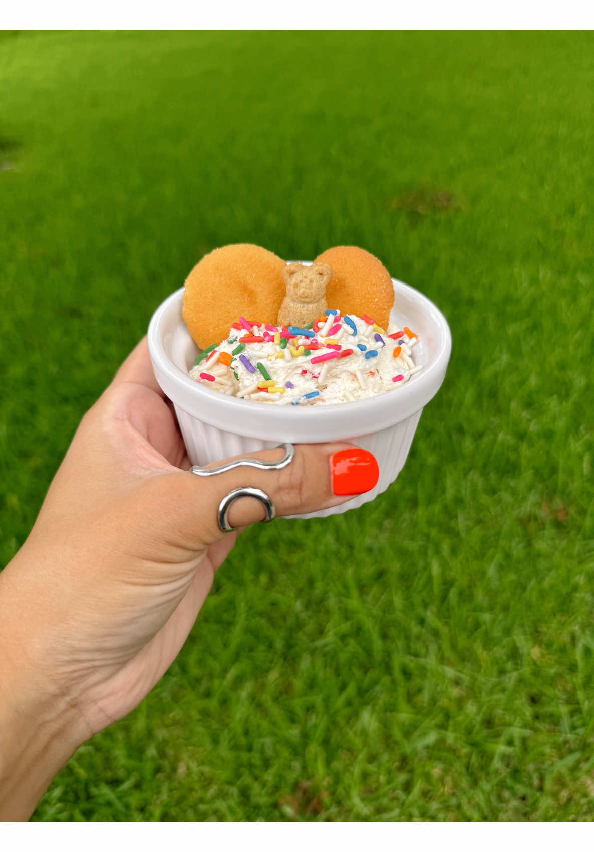 Hand with orange nails and silver rings holding cute creamy dessert with wafers sprinkles and