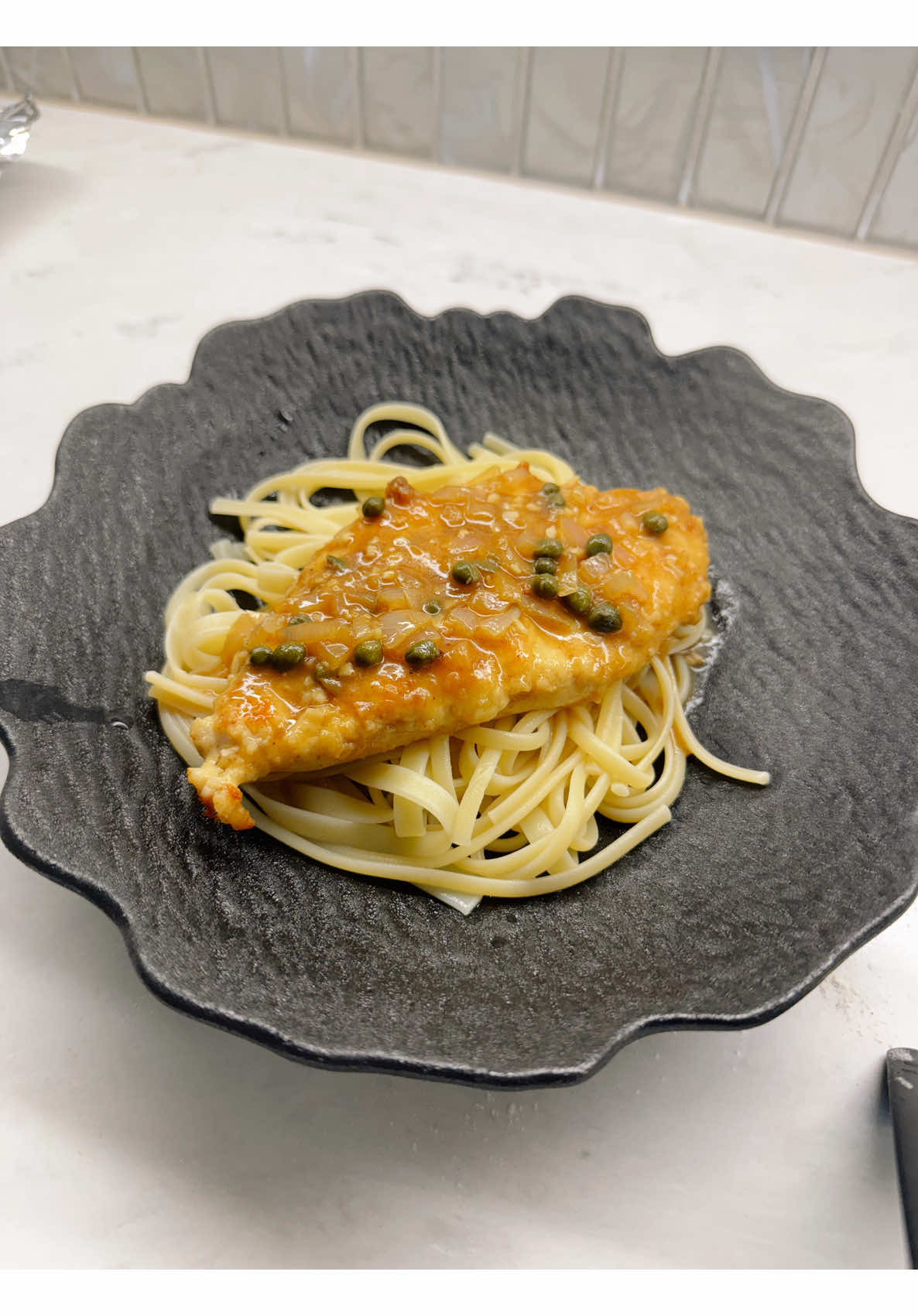 Golden fried chicken cutlet with caper onion sauce linguine on dark plate